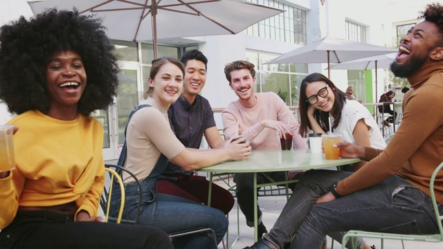 六位千禧一代的朋友坐在街上一家咖啡馆外聊天，对着镜头微笑视频素材