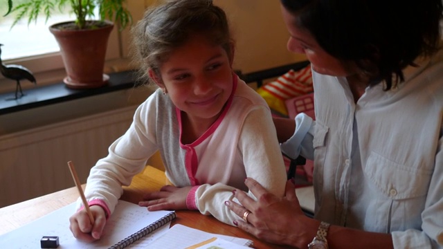 微笑的女孩做数学作业，而坐在桌子旁的母亲在房间里视频素材