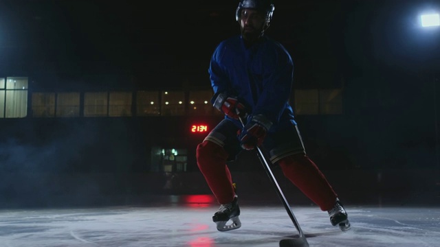 冰场上手持冰球的男子冰球运动员在镜头前直接带球移动，在烟雾中的黑暗背景下直视镜头视频素材
