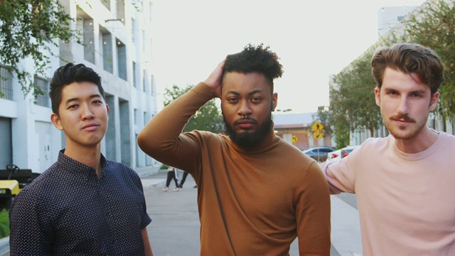 三个年轻的成年男性朋友站在城市的街道上看着镜头，正面，特写视频素材