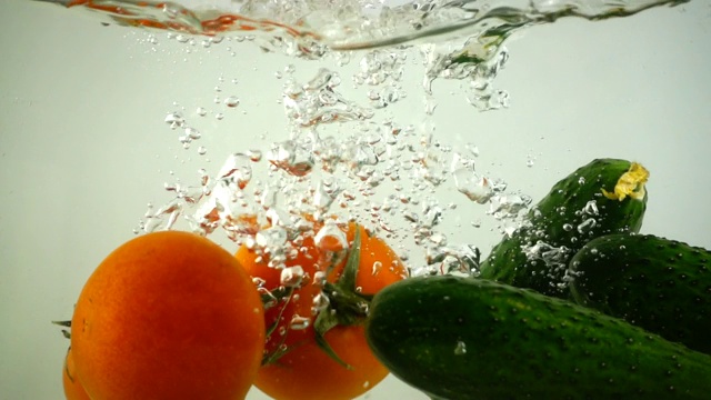 黄瓜和西红柿落入水中。缓慢的运动。视频素材