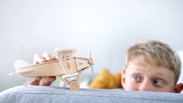 男孩玩木制飞机玩具模型的慢镜头。他把它“落地”在客厅的沙发扶手上。视频素材