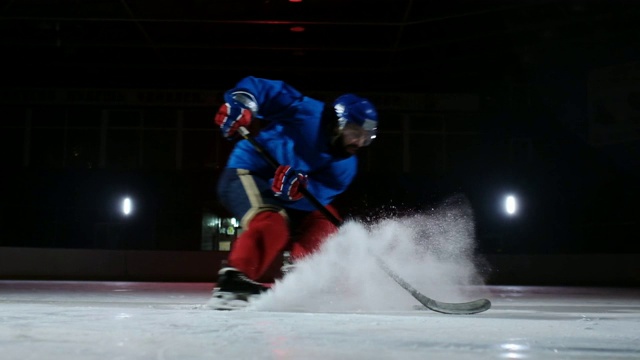 冰球的特写是在冰上的慢镜头中冰球运动员停下来，雪花飞进镜头，他拿起冰球棒视频素材