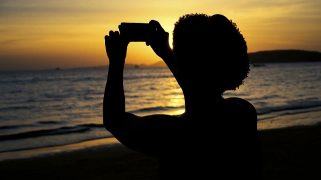 剪影的背影年轻男性旅行背包客与帽子拍照的夏天海滩风景日落-旅游照片瞬间捕捉概念视频素材