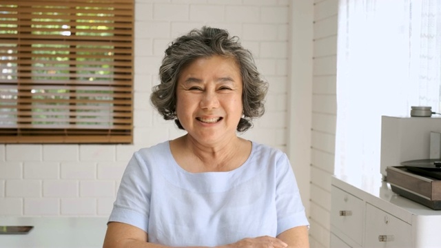 亚洲高级妇女的肖像看着相机和微笑在家里的客厅。快乐的居家养老理念视频下载