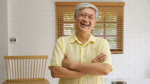 亚洲老年人的肖像交叉一个手臂，看着相机，笑在家里的客厅，快乐的老在家的概念。视频下载