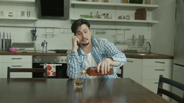 一个男人坐在厨房里拿着一瓶酒视频素材