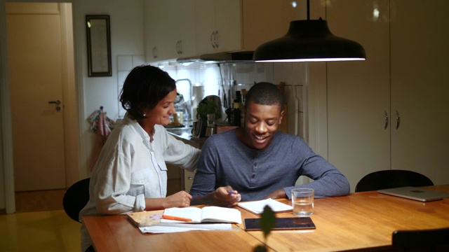 手持拍摄的成熟妇女欢呼养子学习在发光的桌子对厨房视频下载