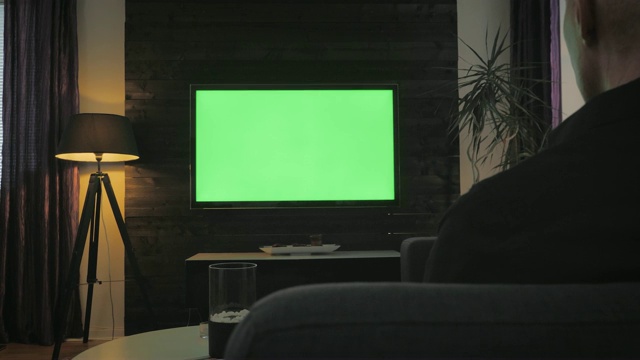 绿屏人在客厅看电视。过肩射击。视频素材