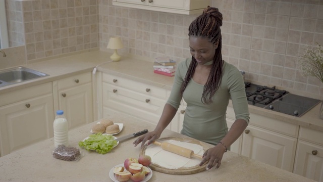 美丽微笑的非洲裔美国妇女在现代厨房里用擀苹果派的擀面杖擀面团。视频素材