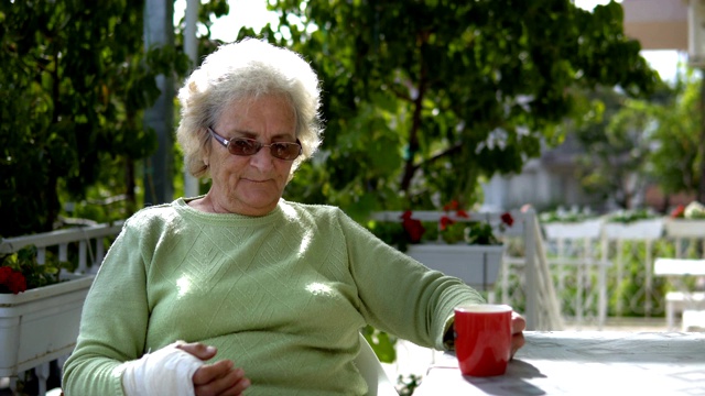 手受伤的老妇人坐在户外喝咖啡视频素材