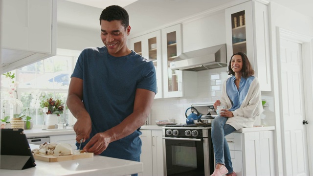 一个年轻的黑人在厨房里准备食物，他的搭档坐在他身后的厨房操作台上视频素材