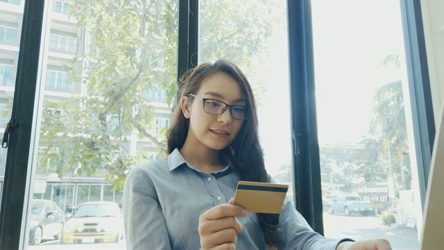 年轻女子持有信用卡，用笔记本电脑进行网上购物支付。家庭网上购物概念与信用卡和笔记本电脑视频素材