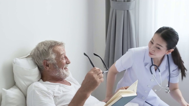 爷爷或老人在床上看书，护士走过来坐在老人旁边检查身体，一起看书视频素材