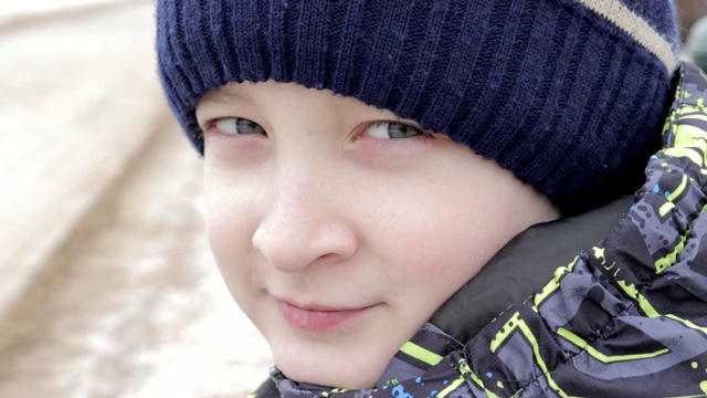 一个美丽的十岁前男孩的近距离肖像与惊人的眼睛坐在公园的长凳上在冬天视频下载