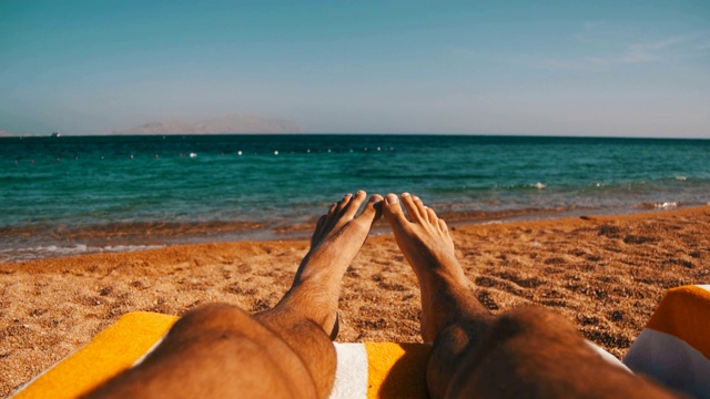 男人的腿躺在海滩太阳躺椅附近的大海视频素材