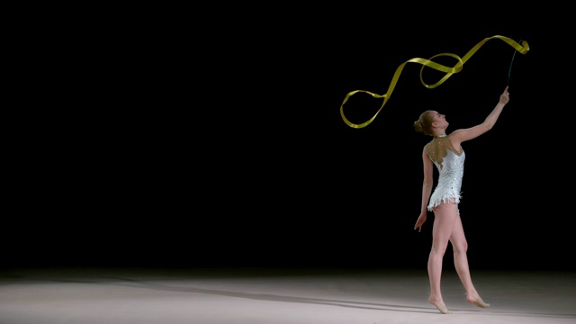 SLO MO LD艺术体操运动员在跳的同时旋转金色的丝带视频素材