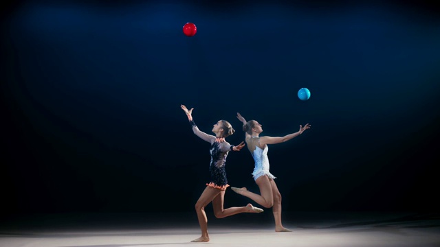 两名艺术体操运动员相对着做劈叉跳跃，同时把他们的球抛向空中视频素材