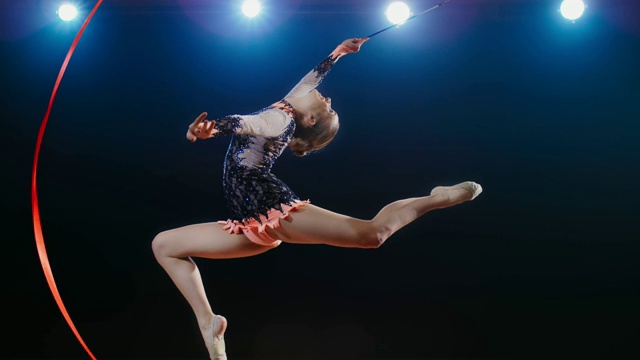 SLO MO LD艺术体操运动员做了一个跳跃，她的头向后倾斜，同时旋转她的红丝带视频下载