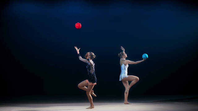 两个艺术体操运动员向相反的方向移动，并在表演劈叉跳跃时接住他们的球视频素材