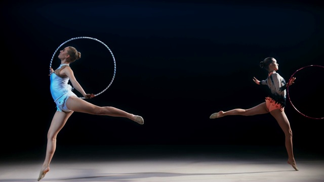 两个艺术体操运动员向相反的方向移动，并表演带有圆环的劈叉跳跃视频素材