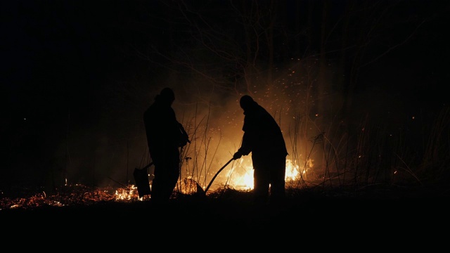 两名消防员在晚上用扑火板扑灭一场火灾视频素材