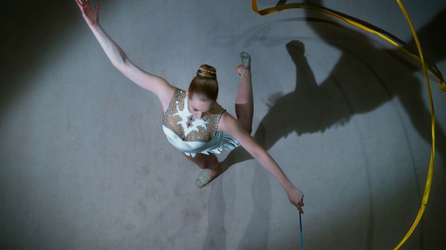 SLO MO LD艺术体操运动员在表演姿态旋转时旋转她的金色丝带视频素材