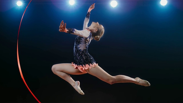 SLO MO艺术体操运动员在做雄鹿跳跃时，在她头上摇摆她的红丝带视频素材