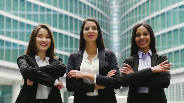 肖像的三个商业女性不同的种族，穿着西装，他们微笑，交叉他们的胳膊。视频素材
