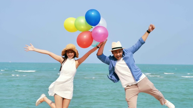 快乐的亚洲夫妇在海滩上拿着彩色气球，生活方式概念，慢镜头。视频下载