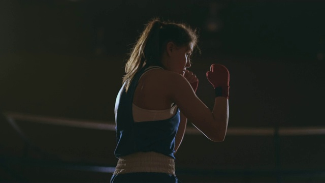 美丽性感的女人拳击手动态打击直接进入相机和向前移动在一个黑暗的背景与背光。替身拍摄视频下载