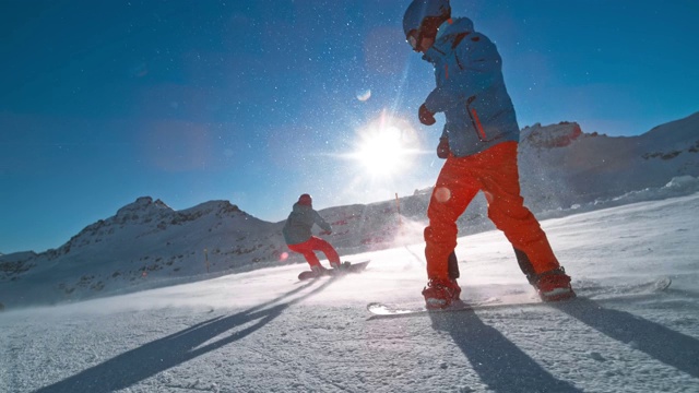 SLO MO TS两名滑雪板运动员在阳光照耀下沿着一个阳光明媚的雪道滑行视频素材