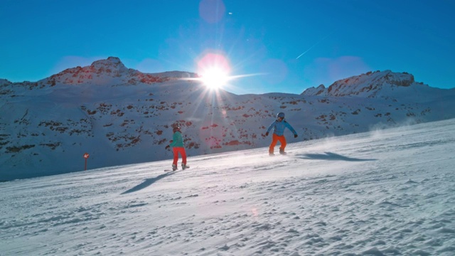 SLO MO TS夫妇骑着滑雪板滑下阳光明媚的山坡视频下载