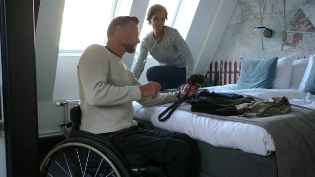 手持拍摄的残疾成年男子在酒店房间用数码相机向女子展示照片视频下载