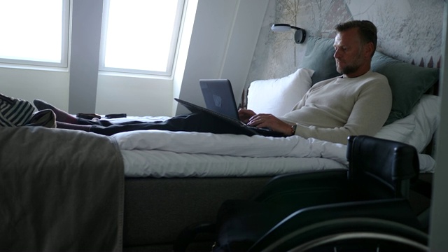 残疾成年商人在酒店房间的床上使用笔记本电脑视频素材