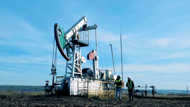 两个人在检查一个工作的油塔。化石燃料，石油工业概念。视频素材