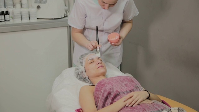 熟练的美容师在水疗沙龙室内躺着的女人脸上敷面膜视频素材