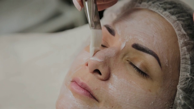 熟练的美容师在水疗沙龙室内躺着的女人脸上敷面膜视频素材