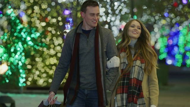 一对夫妇在圣诞节期间提着购物袋走在人行道上的慢镜头/美国犹他州普罗沃视频素材