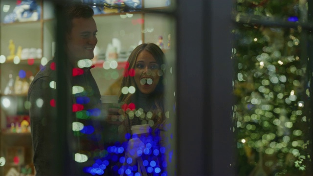 美国犹他州普罗沃，一对夫妇在圣诞节商店的橱窗后面喝酒和欢笑视频素材