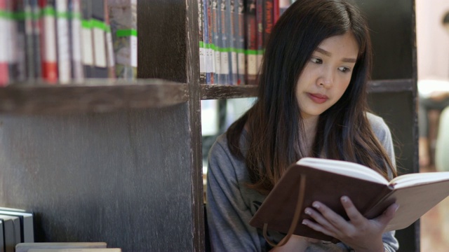 亚洲女学生坐在书架前，在大学图书馆看书。教育的概念。视频素材
