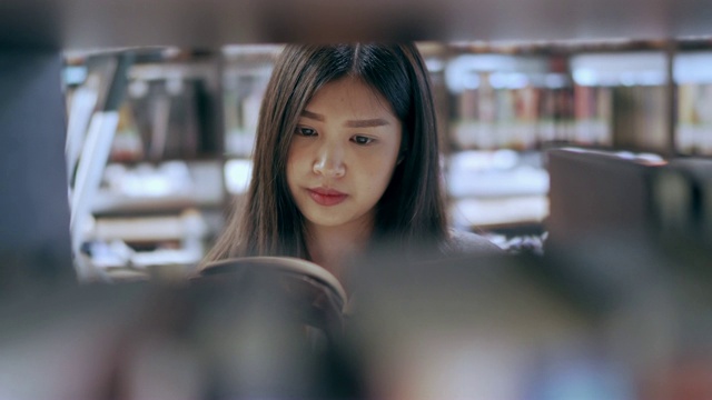 亚洲女学生站在书架后面，在大学图书馆看书。教育的概念。视频购买