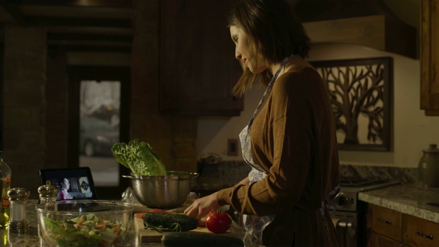 美国犹他州雪松山，一名妇女正在厨房里准备沙拉并观看数字平板电脑视频素材