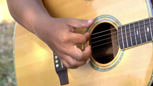 4K视频选择聚焦近距离拍摄的年轻男子手弹奏铜管琴弦的原声吉他。年轻音乐家的手在吉他上弹奏和弦。视频下载