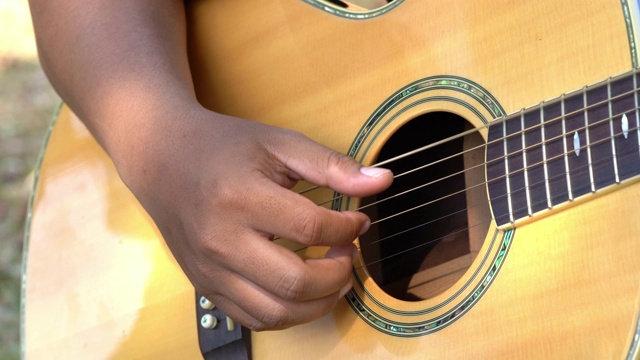 4K视频选择聚焦近距离拍摄的年轻男子手弹奏铜管琴弦的原声吉他。年轻音乐家的手在吉他上弹奏和弦。视频下载