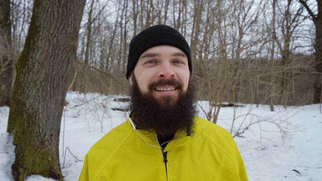 在冬季森林里，一名长着蓝眼睛的大胡子男子对着镜头微笑视频下载