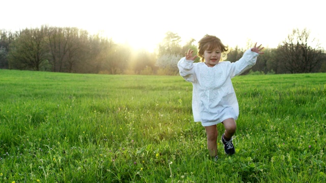一个两岁的小女孩跑向草地上的一棵树，和他一起成长。成长理念，生命流逝，时光流逝。快乐的生活和自由视频素材