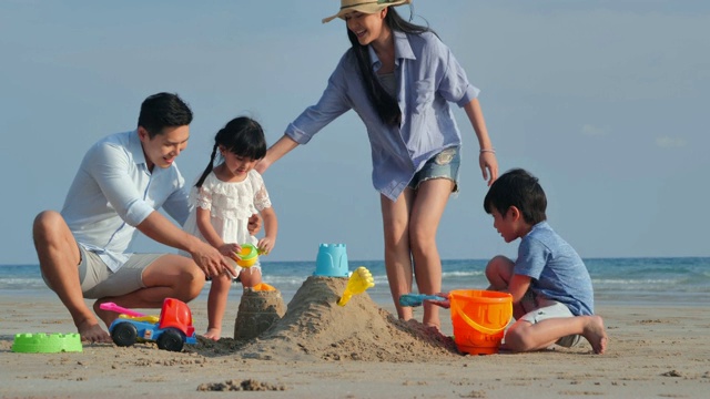 一家人在沙滩上的沙箱里为孩子们玩玩具。快乐的一家人在海滩上享受暑假。假期——iStock视频素材