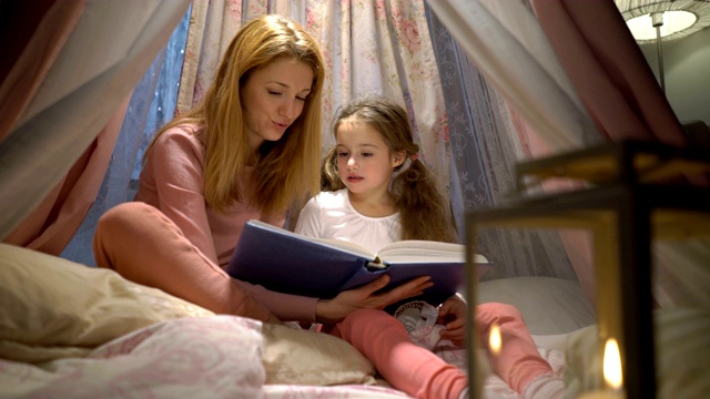 快乐的家庭妈妈和她的小女儿在家里的帐篷里看书视频素材
