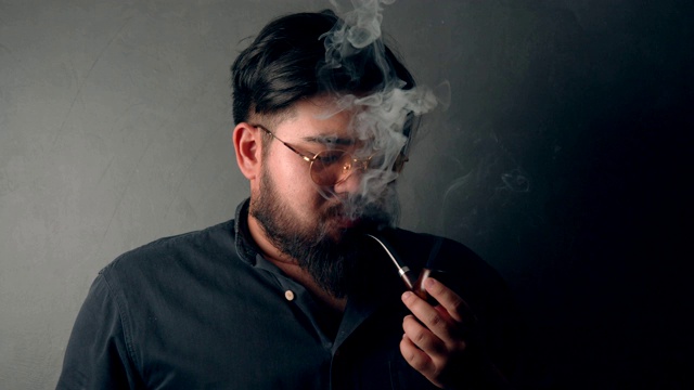 在黑色背景前抽着烟斗的亚洲胡子男子(1)视频素材